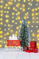 Christmas tree, gift boxes and wooden lettering Merry Christmas on light bokeh background. photo