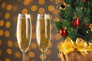 Two wine glasses with bubbly Champagne on blurry sparkling lights background and Christmas tree photo