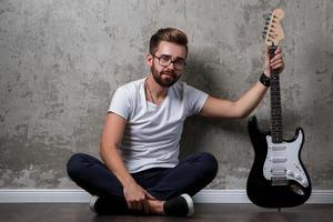 chico barbudo elegante con guitarra contra pared de hormigón foto