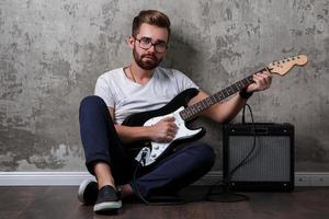 Stylish bearded guy with guitar against concrete wall photo