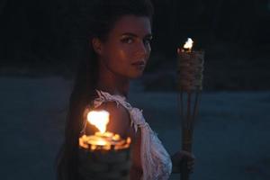 Bride in beautiful wedding dress is holding torchlight on the beach photo