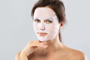 Woman with a sheet moisturizing mask on her face isolated on gray background photo