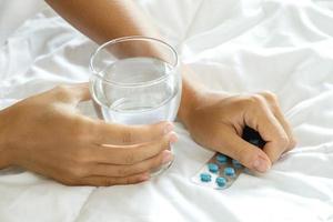 manos femeninas con un vaso de agua y pastillas foto