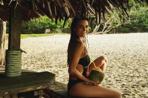 Happy woman is enjoying coconut drink in the beach bar photo
