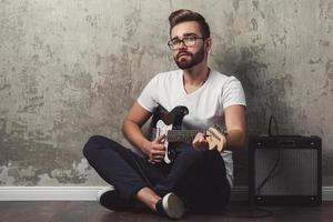 Stylish bearded guy with guitar against concrete wall photo