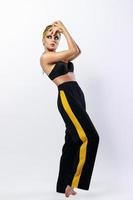 Stylish woman with yellow hair and trackpants on gray background photo