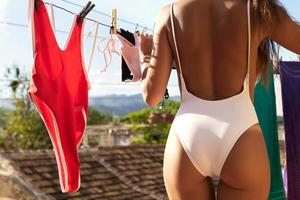 Beautiful woman hanging her wet swimsuits on roof of her house photo