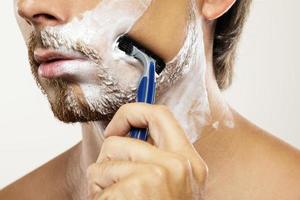 Man with a safety razor and shaving cream on his face photo