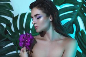 una mujer joven y hermosa con una piel suave y perfecta sostiene flores de orquídeas foto