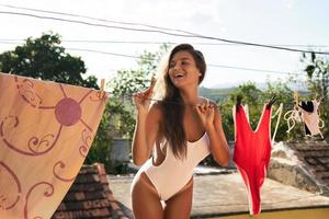 Beautiful woman hanging her wet swimsuits on roof of her house photo