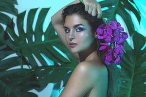 una mujer joven y hermosa con una piel suave y perfecta sostiene flores de orquídeas foto