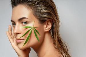 CBD cosmetics concept. Beautiful woman with a cannabis leaf photo