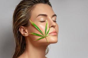 CBD cosmetics concept. Beautiful woman with a cannabis leaf photo