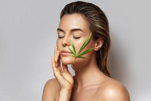 CBD cosmetics concept. Beautiful woman with a cannabis leaf photo