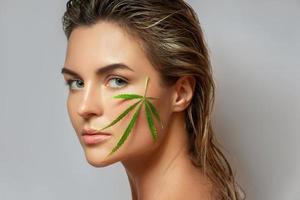 CBD cosmetics concept. Beautiful woman with a cannabis leaf photo