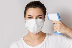 Young woman wearing face mask is measuring body temperature photo