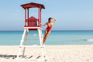 Sexy woman in red swimsuit posing beside a lifeguard tower photo