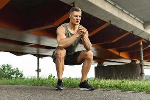 Muscular man is making squats under the bridge during his street workout photo