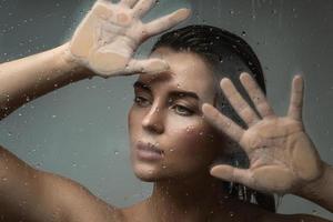 Portrait of beautiful woman captured through wet glass photo