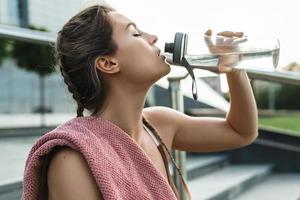 Tired woman drinking water after her fitness workout outdoors photo