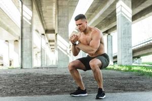 Man is doing squats under the bridge during his street workout photo