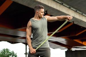 Muscular man during workout with a resistance rubber band on a street. photo