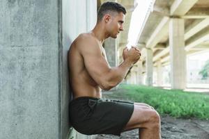 Man is doing wall sit exercise under a bridge during his street workout photo