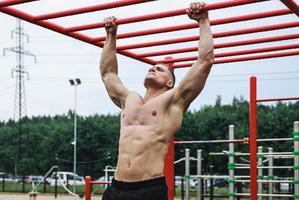 Muscular man doing pull-ups on horizontal bar photo