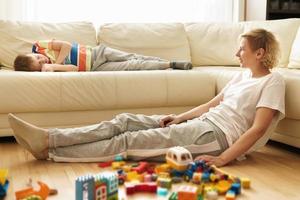Boy lying on the sofa and his mother sitting on the floor after game with a construct toy photo