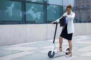 Young and beautiful businesswoman rides electric scooter photo
