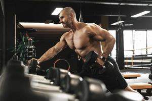 Bodybuilder doing one-arm dumbbell row during his workout in a gym photo