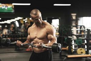 Muscular bodybuilder doing biceps curls with a barbell in the gym photo