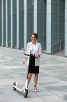 Young and beautiful businesswoman rides electric scooter photo