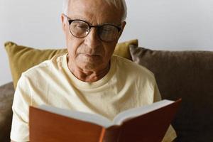 Wise and elderly man is reading book at home photo