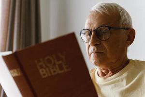 Elderly man reading holy bible at home photo