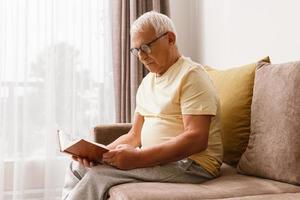 Wise and elderly man is reading book at home photo