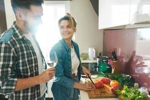 pareja feliz cocinando lanzamiento y bebiendo vino juntos en la cocina foto