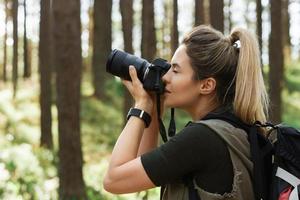 excursionista tomando fotos usando una cámara sin espejo moderna en un bosque verde