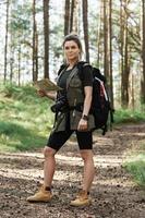 Female hiker with big backpack using map for orienteering in the forest photo