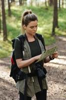 Female hiker with big backpack using map for orienteering in the forest photo