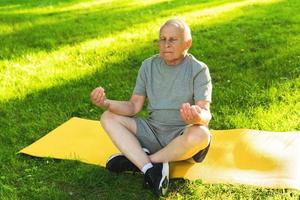 Elderly man meditating during his yoga workout in green city park photo