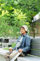 anciano con un longboard sentado en el banco y tomando café en un parque de la ciudad foto
