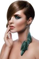 Model in stylish image with sleek hair covering one eye and feather earring photo