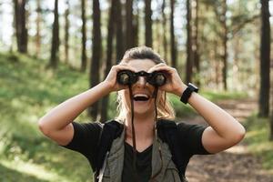 Female hiker is using binoculars for bird watching in green forest photo