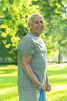 Active elderly man exercising with a rubber resistance band in green city park photo