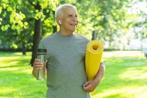 Active elderly man with a exercise mat and bottle of water in green city park photo