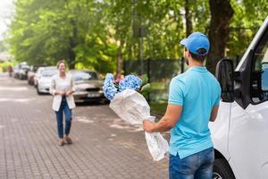 Young delivery man in blue uniform delivers flowers to a woman client photo