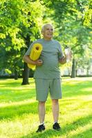 Active elderly man with a exercise mat and bottle of water in green city park photo