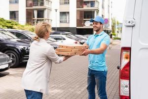 repartidor con uniforme azul entrega pizza a una mujer cliente foto