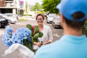 Young delivery man in blue uniform delivers flowers to a woman client photo